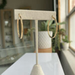 Gold hoop earrings hanging on a white jewelry display stand in a shop window display.