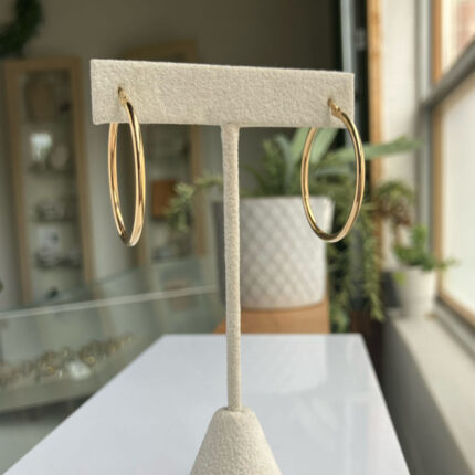 Gold hoop earrings hanging on a white jewelry display stand in a shop window display.