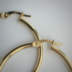 Close-up of gold hoop earrings with hinged clasps, stamped 10KT on the clasp