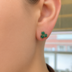 Close-up of a left earlobe with a three-stone green gemstone cluster earring set in gold.