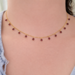Delicate gold chain necklace with small red gemstones evenly spaced around the collarbone area on a light-skinned person.