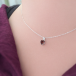 Close-up of a silver chain necklace with a dark red gemstone pendant resting on a woman's collarbone.