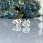 Close-up of two silver screw-back earring backs resting on a reflective surface.