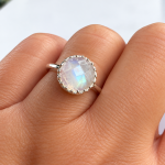 Moonstone ring with a faceted iridescent cabochon set in a silver bezel, worn on a finger.