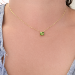 Gold chain necklace with a square green gemstone resting at the collarbone