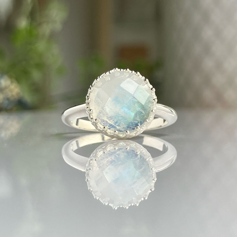 rose cut sterling silver moonstone ringjpeg | Posy Fine Jewellery Toronto Round faceted moonstone ring in a silver bezel with a beaded edge, reflected on a glossy surface.