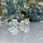 Pair of diamond stud earrings with four-prong settings on a reflective surface.