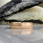 Hammered rose gold wedding band with a reflective surface on a light background.