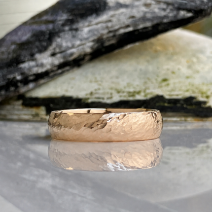 Hammered rose gold wedding band with a reflective surface on a light background.