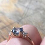 Close-up of a silver ring with a large blue gemstone held between two fingers.
