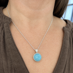 Silver necklace with a round blue gemstone pendant resting on the chest.