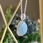 Silver chain necklace with a blue oval pendant hanging in front of a blurred background.