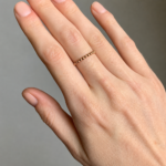 Close-up of a hand wearing a thin gold beaded ring on the ring finger.
