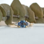 Gold ring with an oval blue sapphire and diamond accents, set on a light surface.