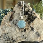 Two silver chain necklaces with large blue circular pendants draped over a rough rock.
