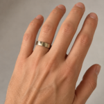 Close-up of a hand showing a brushed silver ring on the ring finger, the focus on the ring and knuckles.