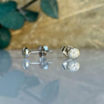 Diamond stud earrings with silver settings resting on a reflective surface