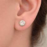 Small round stud earring with a clear gemstone in a silver bezel set on the earlobe.