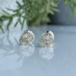 Pair of silver shell-shaped cufflinks with a polished, scalloped design on a reflective surface with a leafy background