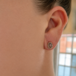 Close-up of a woman's ear wearing a gray gemstone stud with a gold beaded halo.