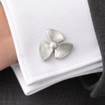 Close-up of a silver three-blade propeller cufflink pinned to a white dress shirt cuff.