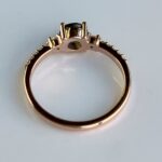 Side view of a rose-gold engagement ring with a dark blue center stone and small diamonds along the band, shown from the side.