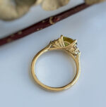 Side view of a gold ring with an ornate setting and a pale green gemstone.