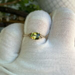 Close-up of an oval green gemstone ring with diamond accents on a white-gloved hand.