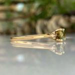Gold ring with a green gemstone set in prongs, photographed on a reflective surface.