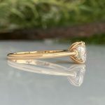 Gold engagement ring with a single oval-cut diamond, shown from the side with a subtle reflection on the surface