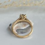 Gold engagement ring with a leaf-style prong setting, resting on a white rock, photographed from the underside showing the polished inner band.