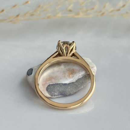 Gold engagement ring with a leaf-style prong setting, resting on a white rock, photographed from the underside showing the polished inner band.