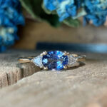Gold ring with a blue oval center stone flanked by two white diamonds on a textured surface.