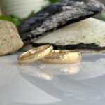 Two hammered gold wedding bands resting on a reflective surface with rocks in the background