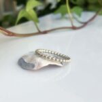 Beaded silver ring resting on a pale shell on a white surface, jewelry photo.