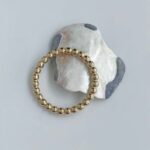 Gold beaded bracelet resting on a white rock with gray patches.