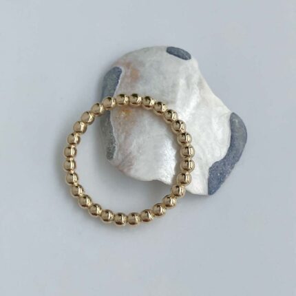 Gold beaded bracelet resting on a white rock with gray patches.