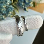 Pair of hammered silver wedding bands resting on a white fabric display surface, close-up