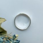 Silver ring on a pale blue surface with dried flowers in the lower-left corner.