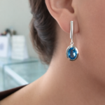 Close-up of a woman's ear wearing a silver drop earring with an oval blue gemstone.