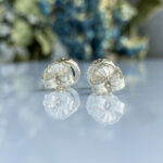 Pair of silver flower-shaped cufflinks with petal details, reflected on a glossy surface.