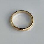 Gold wedding band with a subtle brushed finish on a white background