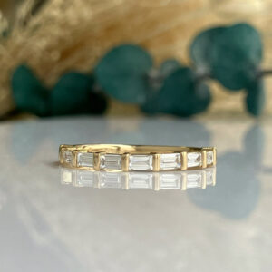Gold band ring with square-cut diamonds set in a channel around the circumference, on a reflective surface.