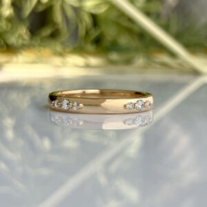 Gold ring with small diamonds set along each side, reflected on a glossy surface.