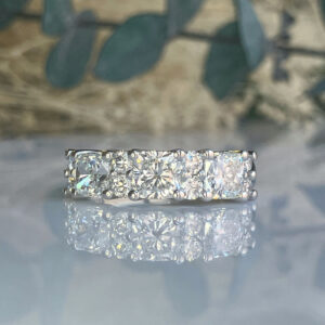 Five-stone diamond ring with prong settings, resting on a reflective surface with a blurred background.