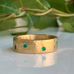 Gold hammered-band ring with evenly spaced green emeralds around the circumference