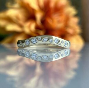 Silver ring set with mixed-cut diamonds arranged along the band, reflected on a glossy surface.