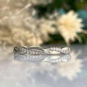 Elegant silver ring with a two-band, twisted design encrusted with small diamonds on a reflective surface