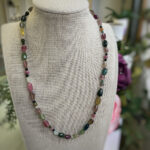 Beaded necklace with irregular multicolored gemstones draped around a beige display bust.