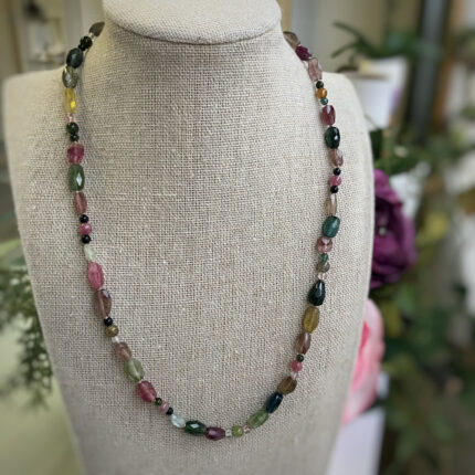 Beaded necklace with irregular multicolored gemstones draped around a beige display bust.